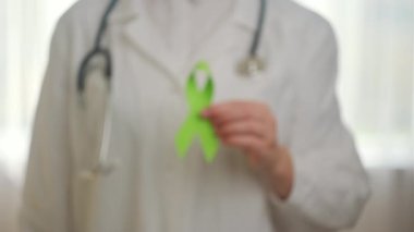 Dünya bipolar günü. Beyaz önlüklü ve steteskoplu küçük yeşil kurdeleli genç bayan doktorlara yakın durun. Akıl sağlığı farkındalığı günü, depresyon, beyin felci. Dünya böbrek günü konsepti