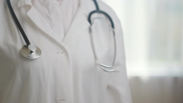 站在医院诊所里 用听诊器把穿着白衣的女医生关在一起 用听诊器显示大拇指向上的姿势 不知名的医务工作者医生表现得像标志 成功的象征 认可的概念 — 图库视频影像