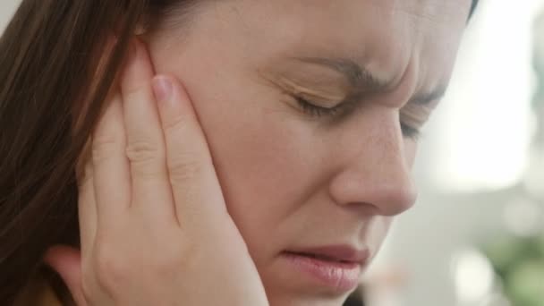 年轻的高加索女性耳痛 头痛且坐在沙发上的侧貌 不健康的疲倦女人得了疼痛的中耳炎 保健和耳鸣概念 — 图库视频影像