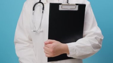 Beyaz önlüklü ve steteskoplu genç bayan doktorun elinde sarı mutlu gülücük, mavi arka planda izole edilmiş, tatmin araştırması, çocuk sağlığı, dünya ruh sağlığı günü, iltifat günü.