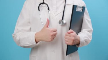 Üzerinde steteskop olan beyaz üniformalı kadın doktorların mavi arka planda izole edilmiş baş parmak hareketi. Bilinmeyen tıp doktoru işaret, başarı sembolü, onay konsepti gibi şeyler gösteriyor.