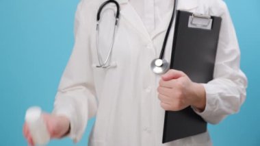Üniformalı kadın doktorun elinde beyaz plastik hap şişesiyle stüdyoda mavi renkli arka plan duvarına reklam için fotokopi alanı olan bir poz verdirdiği bir fotoğraf. Tıp konsepti