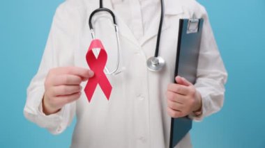 Kırmızı kurdele taşıyan genç bir kadın doktor, mavi arka planda izole edilmiş hastalıklı hastaları destekliyor. Farkındalık, sağlık hizmetleri, yardım ve umut. AID, HIV konsepti