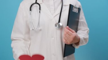 Kırmızı kalp şeklini koruyan steteskoplu üniformalı, mavi arka planda izole edilmiş kimliği belirsiz kadın doktorlara yakın durun. Aşk, donör, dünya kalp günü, dünya sağlık günü, CSR bağışı ve sigorta konsepti