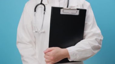 Üniformalı kadın doktorun elinde steteskop, elinde kağıt aile resmi, mavi duvarda izole edilmiş, koruyucu aile, evsiz desteği, koruma, dünya ruh sağlığı günü, sigorta konseptini destekleme