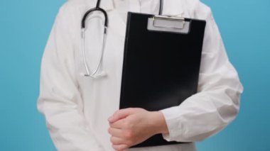 Profesyonel medikal beyaz üniforma ve steteskop giyen genç bayan doktorların el ele tutuşup mavi arka planda izole edilmiş bir şekilde poz verdiği küçük kağıt ev. Sağlık sigortası konsepti