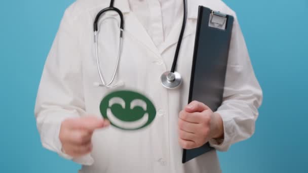 穿着白衣 头戴听诊器 带着绿色快乐微笑 因蓝色背景 满意度调查 儿童健康 世界心理健康日 赞美日而被隔离的年轻女医生的近照 — 图库视频影像