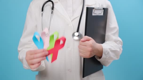 身边的年轻女医生拿着蓝色 粉色等五彩斑斓的小丝带 为人们的生活和疾病提供支持 意识和保险概念 世界癌症日 — 图库视频影像