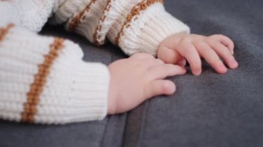 Evdeki rahat kanepeye yaslanmış güzel bebek ellerini kapat. Nazikçe Kafkas bebek eli. Ilık beyaz süveter giyen küçük bebek. Çocukluk kavramı, yeni hayat ve ebeveynlik