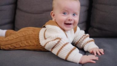 Evdeki rahat kanepede dinlenen, sıcak süveter giyen sevimli beyaz bir çocuğun portresi. Oturma odasındaki rahat koltukta gülümseyen bebek. Çocuk bakımı ve çocukluk konsepti