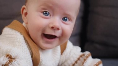 Evdeki rahat koltukta dinlenen beyaz kazaklı, gülümseyen, yeni doğmuş güzel bir bebeğin yakın portresi. Kameraya bakan oldukça huzurlu bir çocuk. Mutlu çocukluk kavramı