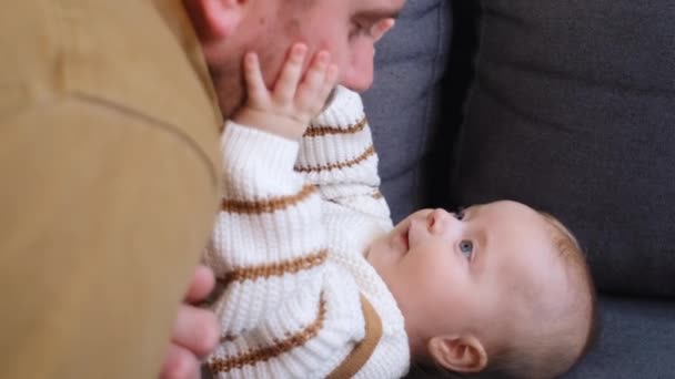 亲热的年轻父亲爱抚着可爱的幼儿 开心的笑着在舒适的沙发上放松 关心着快乐的爸爸和小男孩在家里拥抱在一起玩耍 — 图库视频影像