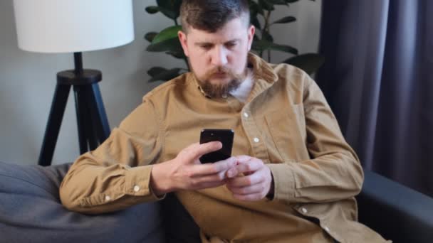 Задумчивый Серьезный Бородатый Молодой Человек Смотрящий Экран Смартфона Имеющий Проблемы — стоковое видео