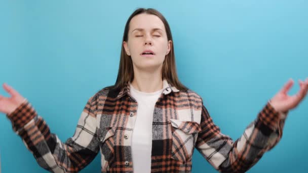 スピリチュアルな静かな若いブルネットの女性の肖像画は ヨガで手を広げているシャツを着て ジェスチャーリラックス瞑想は落ち着いて スタジオでパステルブルーの背景壁の上に隔離されたポーズを試みます — ストック動画