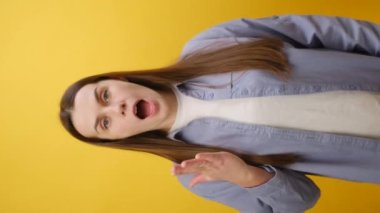 Dikey çekimde, beyaz gömlekli genç bir kadın megafonla çığlık atıyor indirimli satışlar, acele edin, stüdyodaki pastel sarısı arka plan duvarına izole edilmiş pozlar verin.
