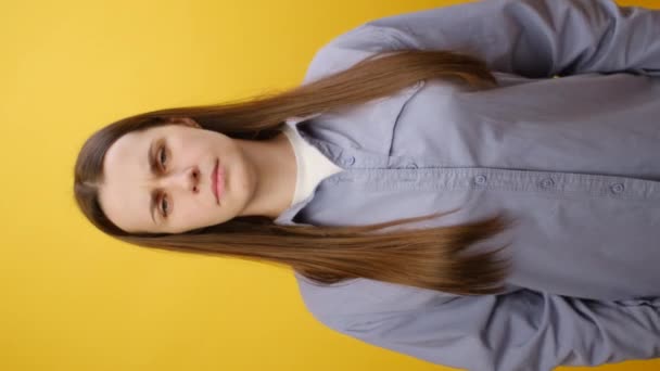 真剣な若い白人女性の垂直ビデオ 赤い不満の悲しみの顔の絵文字を保持し スタジオの明白な黄色の背景の壁の上に隔離されています コンセプト ストレス ネガティブな感情 — ストック動画