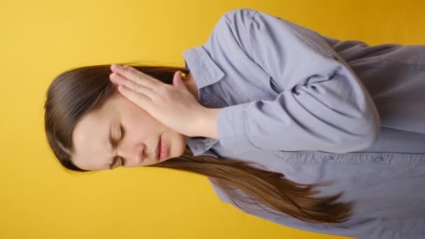 耳の痛みや耳鳴りに苦しむ悲しい若い白人女性の垂直ビデオは 黄色いスタジオの背景の上に隔離されています 卵巣の原因は 耳ワックスを構築し 罪の感染症を含みます — ストック動画
