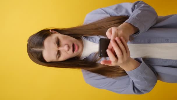 Pionowe Ujęcie Podrażnionej Młodej Białej Kobiety Noszącej Koszulę Używającej Telefonu — Wideo stockowe