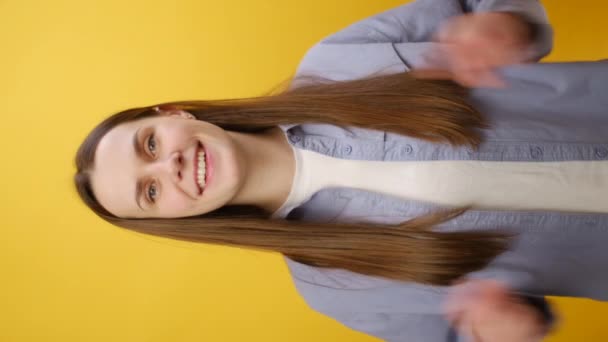 美しい幸せなブルネットの若い女性の垂直ビデオ カメラを指し 喜んで笑顔で 私たちはあなたを必要とし 方向を示し 黄色のスタジオの背景に隔離されていることを意味します — ストック動画