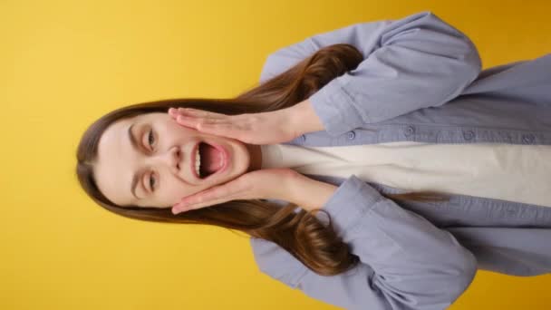 驚いたかわいい若い女性25代の垂直映像は ジェスチャーのような親指を示す青いシャツを着て スタジオの黄色の背景の壁の上に隔離された 人々の感情ライフスタイルの概念 — ストック動画