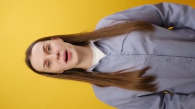 Çekici, pozitif gülümseyen genç bir kadının el hareketlerini gösteren, sarı stüdyo arka planında izole edilmiş bir poz veren dikey videosu. Tebrik ederim. Motivasyon teşvik edici
