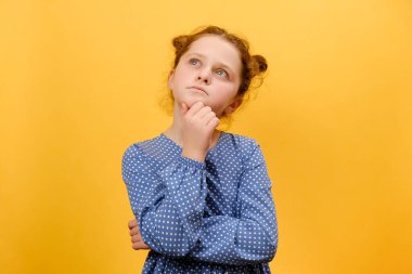 Düşünceli ergen kız çocuğunun portresi. Fikir üzerine kafa yoruyor, çenesine dokunuyor. Stüdyoda sade sarı arka plan duvarında izole bir şekilde poz veriyor. Hmm, bir düşünelim. Düşünceli ve beyin fırtınası konsepti