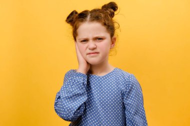 Kulak ağrısından muzdarip mutsuz çocuk portresi. Stüdyodaki sarı arkaplan duvarında izole bir poz veriyor. Kulak ağrısına kulak iltihabı, kulak kiri, sinüs enfeksiyonu neden olur.