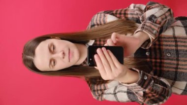 Dikey olarak genç bir bayanın el sallayıp kırmızı duvarda izole edilmiş bir şekilde el salladığı görüntüler. Seni görmek ne güzel. Mutlu duygular. Video konuşması yapan güzel bir kız online akıllı telefon..