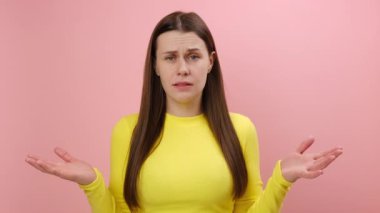 Sinirli genç bir kadın, sarı kazak giyiyor, öfkeyle ellerini kaldırıyor ve neden, ne istiyorsun diye bağırıyor, kavga ediyor, kameraya bakıyor, stüdyodaki pembe arka plan duvarında izole edilmiş bir şekilde poz veriyor.