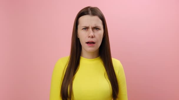 驚くべき表情で立っている怖い若い女性の肖像画 大きな目を持つカメラを見て 非常に驚き スタジオでピンクの背景の壁に隔離された黄色いセーターを着ています — ストック動画
