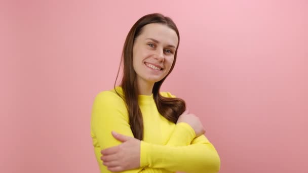 スタジオのピンク色の背景の壁に隔離された黄色のセーターを身に着け 自分自身を抱きしめ 利己的で 自分自身を抱きしめている穏やかな美しい美しい若い女性の肖像画 私は自分自身を愛する — ストック動画