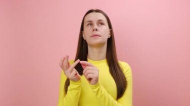 Düşünceli genç bir kadının portresi parmaklarını bükmek, düşünme ve hesaplama ile bakmak, sarı kazak giymek, stüdyodaki pembe renkli arka plan duvarında izole edilmiş poz vermek.