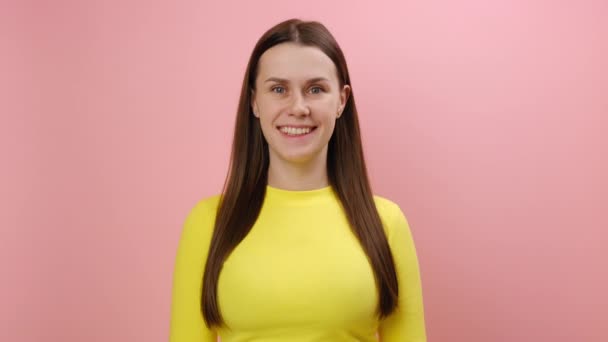 快乐迷人的年轻女性25岁点头表示同意 表示同意 用积极的目光看着相机 穿着黄色毛衣 在工作室里用浅粉色的背景墙把自己隔离起来 — 图库视频影像
