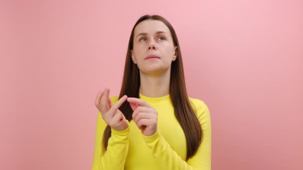 思慮深い美しい若い女性の肖像画 指を曲げ 計算して見て イエローセーターを着て スタジオでピンク色の背景の壁の上に隔離しました — ストック動画