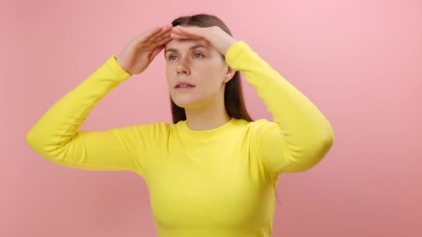 ピンクの背景の壁に隔離された黄色いセーターを身に着けている 注意深い視野 遠い将来のコンセプトとの距離を調べ 彼女の目に手のひらを握っている集中した若い女性の肖像画 — ストック動画