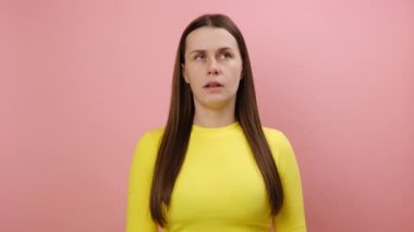 Sıkılmış genç beyaz bir kadının portresi yanaklarında geziyor, mutsuz görünüyor, sıkıcı toplantılardan hoşlanmıyor, sarı kazak giyiyor, stüdyodaki pembe renkli arka plan duvarına izole edilmiş poz veriyor.