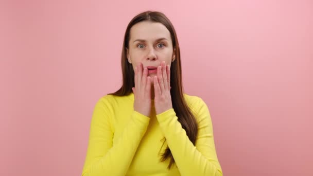 ショックを受けた若い女性 驚きで開いたカメラを見て 肯定的な驚きを表し 親指を示し 黄色のセーターを着て スタジオでピンク色の背景の壁に隔離されたポーズ — ストック動画
