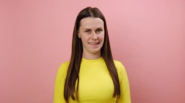 Kurnaz, kurnaz, gülümseyen, beyaz bir kadın kameraya bakıyor, bir şeyler planlıyor, birine şaka yapıyor, sarı kazak giyiyor, stüdyodaki pembe renkli arka plan duvarına izole edilmiş bir şekilde poz veriyor.