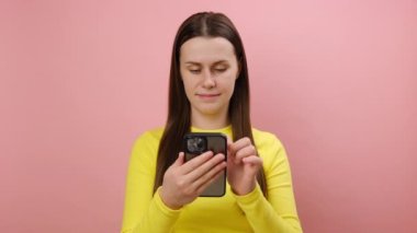 Sosyal ağda cep telefonuyla yazı okuyan, şaşırmış görünen, sarı kazak giyen, stüdyodaki pembe renkli arka plan duvarının üzerine izole edilmiş bir şekilde poz veren genç kadın hayrete düştü. Sohbet kavramı
