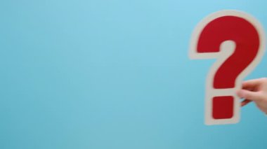 Soru işareti sembolü. Büyük kırmızı soru işareti kağıdını tutan bir kadının elini kapatın. Stüdyoda mavi arkaplan duvarına izole edilmiş ve promosyon içeriği için fotokopi alanı var. Soru konsepti