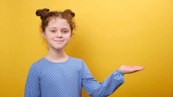 子供のための商品 愛らしい小さな少女の子供の肖像画は 広告のためのコピースペースとスタジオの黄色の背景の壁に隔離された何かを示しています — ストック動画