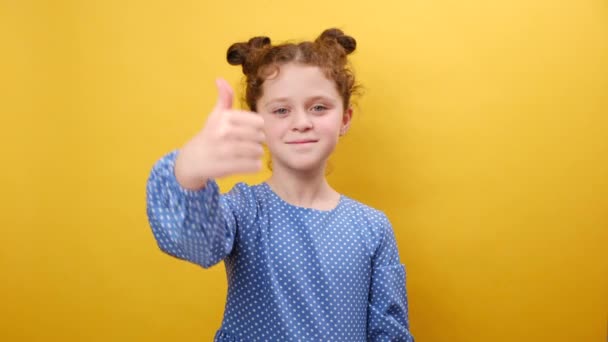 喜欢和认可 图片上可爱的积极的小女孩竖起大拇指 对着相机真诚微笑 在工作室里把黄色背景与广告空间隔离在一起 — 图库视频影像