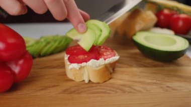 Genç bayana yakın durmak sağlıklı kahvaltı hazırlar ya da tahta tahtada atıştırmalık bir şeyler hazırlar. Avokadolu yumuşak peynir, baget ekmekli domates. Sağlıklı gıda konsepti