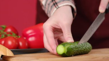 Mutfaktaki ahşap tahtada taze yeşil salatalık kesmeye yakın durun. Bilinmeyen bir kadın salatalığı peynirli ve domatesli sandviç için dilimliyor. Salatalığı uzunlamasına dilimle. Çevre dostu organik öğle yemeği.