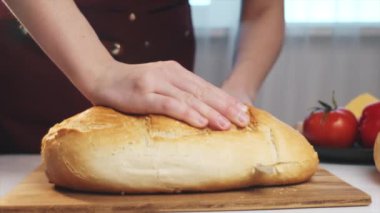 Ev mutfağında tahta tahtada ekmek kesen kadın ellerini kapatın. Sandviç yapmak için ekmek dilimliyorum. Sabah kahvaltısı hazırlıyorum. Yemek konsepti. Yavaş çekim