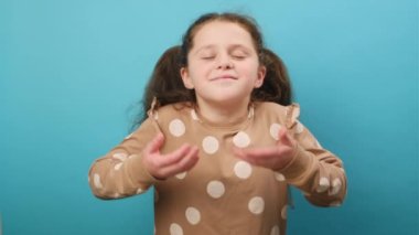 Mutlu reşit olmayan kız portresi rahatlatıcı, gülümseyen, gözleri kapalı çocuk huzurlu bir şekilde nefes alıyor, hoş bir koku alıyor, stüdyodaki mavi arka plan duvarında izole bir şekilde poz veriyor.