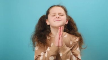 Tanrı 'ya dua eden, dua eden, kameraya bakan, stüdyodaki sade mavi arka plan duvarına izole edilmiş şirin, huzurlu bir genç kızın portresi. Samimi çocukların inancı. Din kavramı