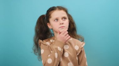 Düşünceli reşit olmayan bir kızın portresi. Fikir üzerine kafa yoruyor, çenesine dokunuyor. Stüdyodaki sade mavi arka plan duvarında izole bir şekilde poz veriyor. Hmm, bir düşünelim. Düşünceli ve beyin fırtınası konsepti