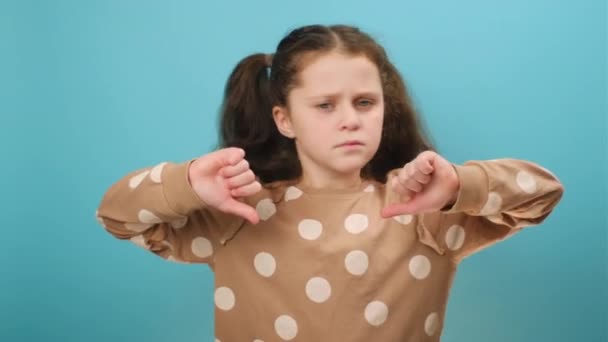 未成年少女的画像 双手放下大拇指 鬼鬼祟祟 在工作室的浅蓝色背景墙上摆出孤立的姿势 不喜欢的概念 情绪化的孩子不赞成某事 — 图库视频影像