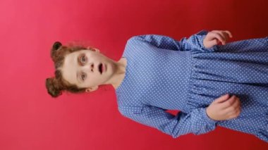 Şok olmuş küçük kızın yüzünü ellerle örttüğü dikey video, kırmızı arka planda izole edilmiş poz, çocuk korku filmi, film, tepki, yüz ifadesi. Çocuklar ve insan duyguları kavramı